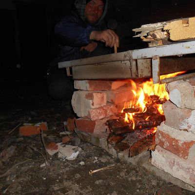 2018 04 : Vítězslav Špalek po práci na stavbě vaří večeři na peci postavené z vybouraných cihel a rozvodné desky. (fotografie Ivan Mečl)